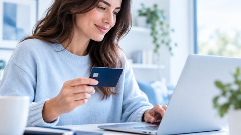 Une personne consulte un ordinateur portable, une carte bancaire à la main.